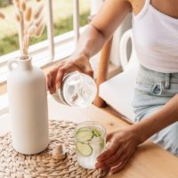 woman in white tank top pouring water on clear drinking glass